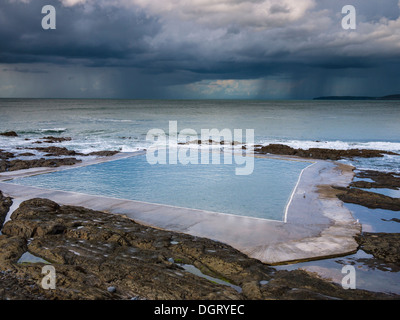 Der Rock Pool Swimmingpool im Westward Ho! Und ein Sommerregensturm über dem Atlantik in der Ferne an der Küste von North Devon, England. Stockfoto