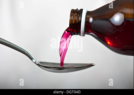 Husten Sirup wird aus einer braunen Glasflasche auf einem Löffel gegossen. Stockfoto