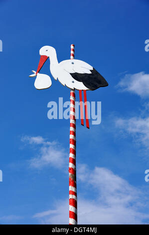 Storch auf einem roten und weißen Pfosten vor blauem Himmel, platziert vor dem Haus eines jungen Ehepaares, fränkische tradition Stockfoto