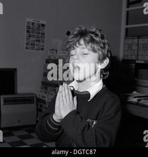 Junge Kind christlicher Glaube betende Augen geschlossen Hände halten im Gebet Grundschule Klassenzimmer vintage retro schwarz-weiß Bild Foto Llanwrda Carmarthenshire Wales UK Great Britiain1988 KATHY DEWITT Stockfoto