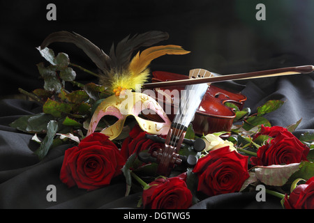 Violine, eine Maske und eine Rose auf einem schwarzen Hintergrund Stockfoto
