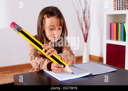 Kleines Mädchen in ihrem Haus mit einem riesigen Bleistift schreiben Stockfoto