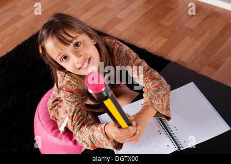 Kleines Mädchen in ihrem Haus mit einem riesigen Bleistift schreiben Stockfoto