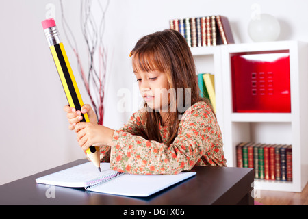 Kleines Mädchen in ihrem Haus mit einem riesigen Bleistift schreiben Stockfoto