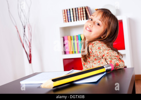 Kleines Mädchen in ihrem Haus mit einem riesigen Bleistift schreiben Stockfoto