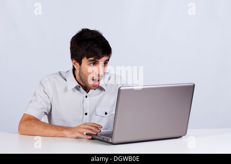 junger Mann schockiert mit etwas, das er auf seinem Laptop zu sehen Stockfoto