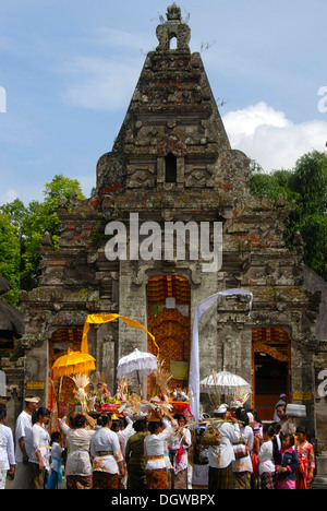 Bali-Hinduismus, gläubige Frauen, gekleidet in festliche Kleidung tragen Angebote und Sonnenschirme, Tempelturm Stockfoto