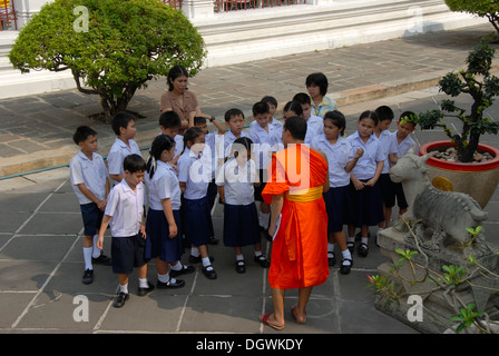 Theravada-Buddhismus, Mönch als Führer einer Schulklasse, orangefarbene Gewänder, Schülerinnen und Schüler in Schuluniformen, Wat Arun, Bangkok Stockfoto