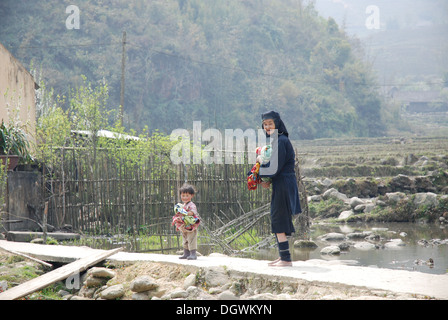 Schwarze Hmong Stämme Frau die Wäsche mit einem Kind Helfer in Cat Cat Dorf in der Nähe von Sapa in Vietnam Stockfoto