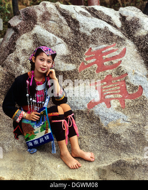 Miao junge Frau trägt einen ethnische Tracht vor Felsen mit chinesischer Inschrift, Hainan, China, Asien Stockfoto