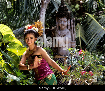 Balinesische Tänzerin in einem traditionellen Kostüm vor eine Steinstatue Candi Dasa, Bali, Südostasien, Indonesien Stockfoto