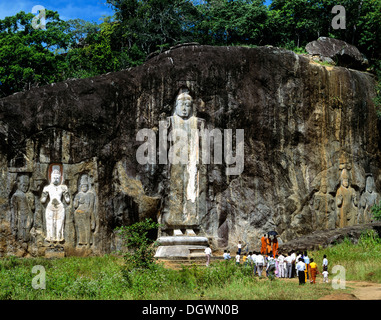 Buduruvagala, Rock von buddhistischen Skulpturen, Mönche und Touristen stehen vor der Deepangkara Buddha-Statue, Buduruvagala Stockfoto