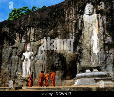 Buduruvagala, Rock von buddhistischen Skulpturen, Deepangkara Buddha-Statue, buddhistische Mönche stehen vor den Statuen des Stockfoto