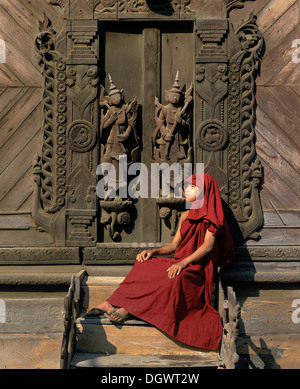 Mönch sitzt vor einer geschnitzten Teak Tür, Shwe In Bin Kyaung Kloster, Mandalay, Mandalay-Division, Myanmar, Burma Stockfoto