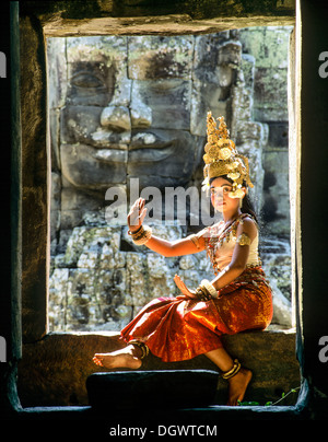 Tempel-Tänzerin oder Apsara sitzen in einem Fenster vor einem Gesicht Turm am Bayon-Tempel, UNESCO Weltkulturerbe Stockfoto