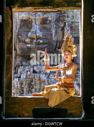 Tempel-Tänzerin oder Apsara sitzen in einem Fenster vor einem Gesicht Turm am Bayon-Tempel, UNESCO Weltkulturerbe Stockfoto