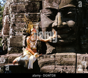 Tempel-Tänzerin oder Apsara sitzt vor einem Gesicht Turm an Angkor Thom, Bayon Tempel, UNESCO Weltkulturerbe Stockfoto