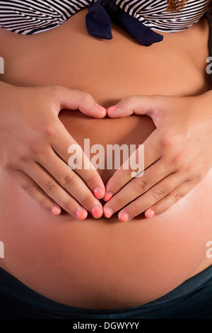 Blick auf einen schwangeren Bauch mit Händen bilden eine Herzform. Stockfoto