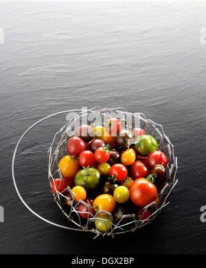 Verschiedene wilde Tomaten in einen Drahtkorb, auf einer Tafel Stockfoto