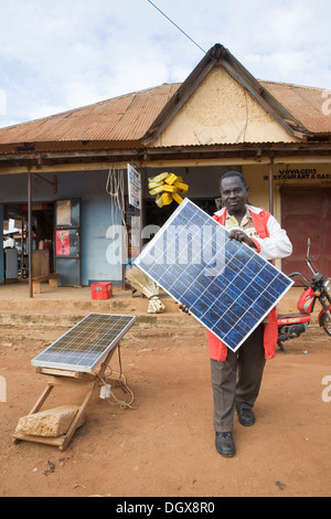 Herr Tinkasimire, Besitzer eines elektrischen Shop bietet Produkte wie Premier Modul Sonnenkollektoren, Masindi, Uganda, Afrika Stockfoto