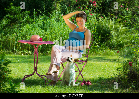Schwangere Frau sitzt in einem Garten mit Hund Stockfoto