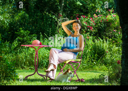 Schwangere Frau sitzt in einem Garten mit Hund Stockfoto