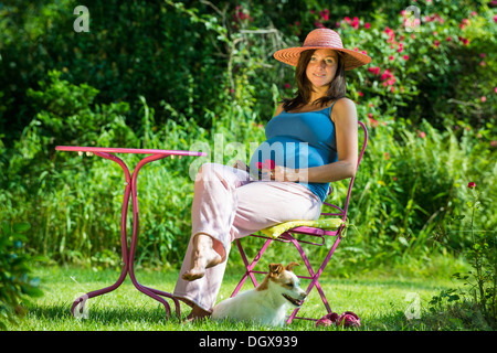 Schwangere Frau sitzt in einem Garten mit Hund Stockfoto