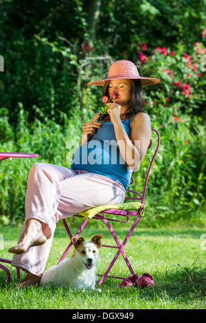 Schwangere Frau sitzt in einem Garten mit Hund Stockfoto