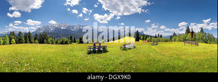 Entspannen Sie sich auf eine Bank in der Mitte eine Blumenwiese mit Panoramablick auf das Wetterstein-massiv mit den Alpen Wanderer Stockfoto