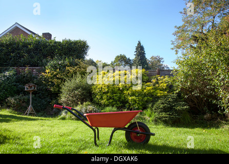 Rote Schubkarre in einem sonnigen s englischen Garten. Stockfoto