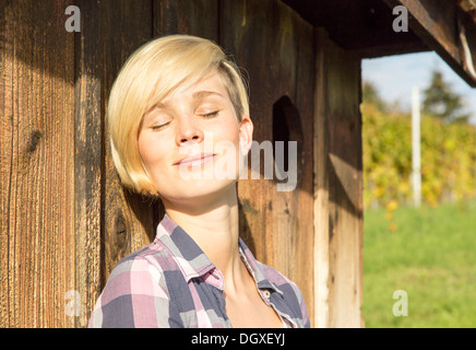 Natürlich aussehende Frau lehnt sich an die Wand einer Hütte und entspannt Stockfoto