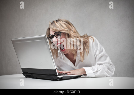 Böse blonde Frau schreiend gegen einen laptop Stockfoto