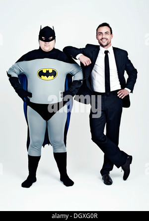 Sportlicher Mann in einem Anzug neben einem dicken Mann gekleidet wie ein Superheld Batman Stockfoto