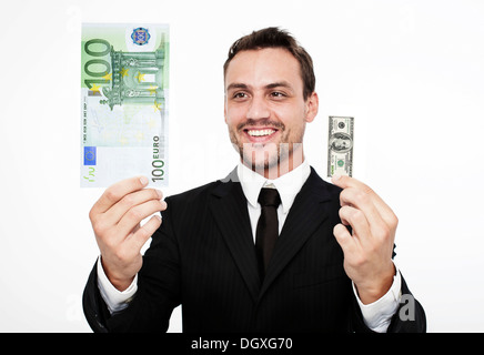 Lächelnde junge Mann trägt einen Anzug hält eine große 100-Euro-Banknote und eine kleine 100 Dollarschein, Österreich Stockfoto