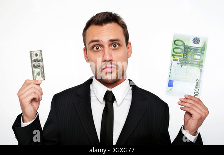 Frustrierte junge Mann trägt einen Anzug hält einen kleinen 100 Dollar-Schein und einen großen 100 Euro-Banknote, Österreich Stockfoto