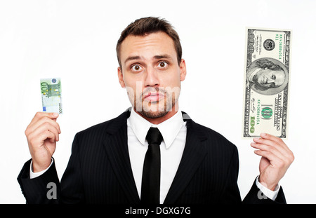Frustrierte junge Mann trägt einen Anzug hält eine kleine 100 Euro-Banknote und einen großen 100 Dollarschein, Österreich Stockfoto