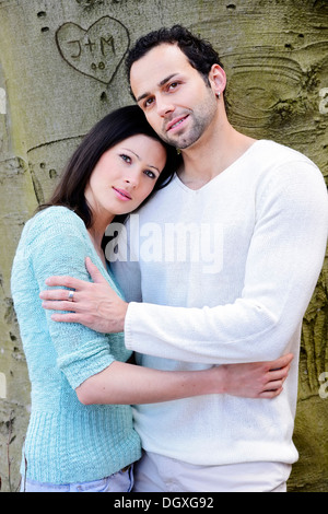 Junge Frau stützte sich auf die Schulter eines jungen Mannes vor einen Baum mit einem geschnitzten Herzen, Österreich Stockfoto
