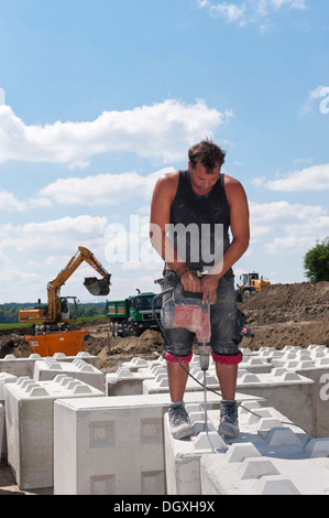 Arbeiter bohrende von Löchern in Steinblöcke, die auf einer Baustelle eingesetzt werden Belastungstests auf einer Baustelle in Fridolfing Stockfoto
