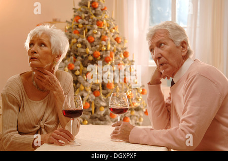 Älteres Paar sitzt an einem Tisch mit Gläsern Rotwein, verärgert, vor einem Weihnachtsbaum suchen Stockfoto