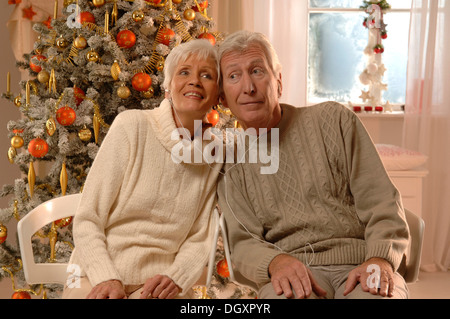Älteres Paar mit Kopfhörer sitzt vor einem Weihnachtsbaum Stockfoto