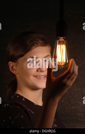 Junges Mädchen mit einer leuchtenden Glühbirne in der Hand lächelnd Stockfoto