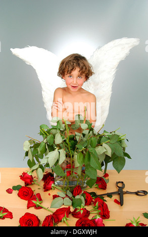 Junge mit Engelsflügeln, nach dem die Köpfe einen Strauß Rosen mit einer großen Schere schneiden Stockfoto