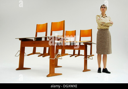 Strenge Lehrerin stehen neben alten Schulbänke mit orange Stühle Stockfoto