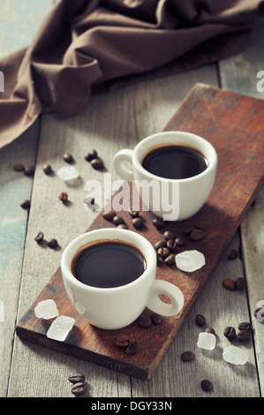 Kaffee in Tassen mit Kaffeebohnen und Weißzucker auf Vintage Holz-Hintergrund Stockfoto