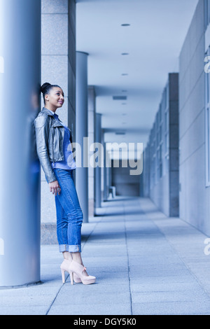Junge Afro-amerikanische Frau in voller Länge, Höhenplan, stützte sich auf Gebäude Stockfoto