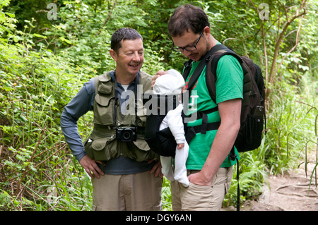 Vater und Sohn tragen sein kleines Baby im Tragetuch genießen Sie einen Spaziergang auf dem Lande Stockfoto