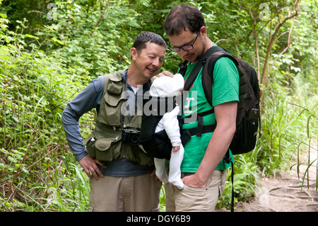 Vater und Sohn tragen sein kleines Baby im Tragetuch genießen Sie einen Spaziergang auf dem Lande Stockfoto