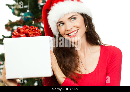 Eine lächelnde schöne Frau trägt eine Weihnachtsmütze und halten einen großen weißen Weihnachtsgeschenk und Kopie-Raum zu betrachten. Isoliert auf w Stockfoto