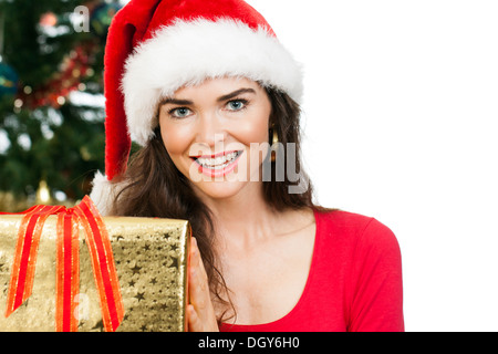 Nahaufnahme einer schönen lächelnden Frau trägt eine Weihnachtsmütze hält eine schöne goldene Weihnachtsgeschenk und Blick in die Kamera. Isola Stockfoto