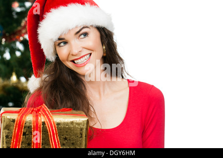 Eine schöne glückliche Frau mit Santa Hut hält eine schöne goldene Weihnachtsgeschenk. und Kopie-Raum zu betrachten. Isoliert auf wh Stockfoto